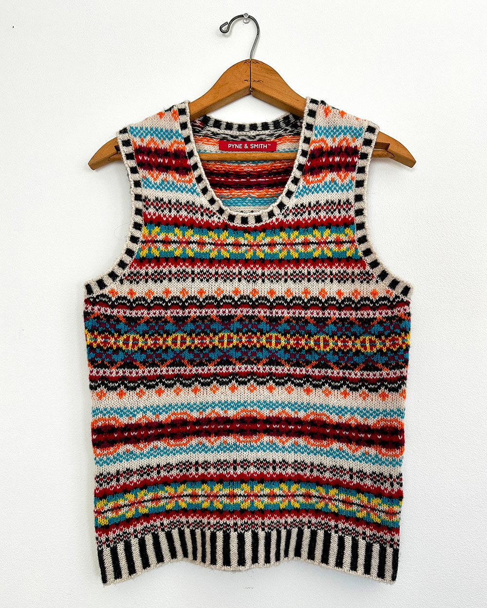 A colorful Fair Isle wool vest hangs on a white wall