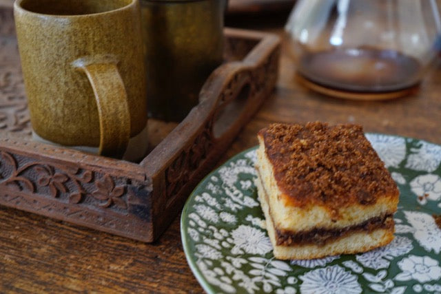 A slice of crumb cake and a cup of tea are on a wooden table