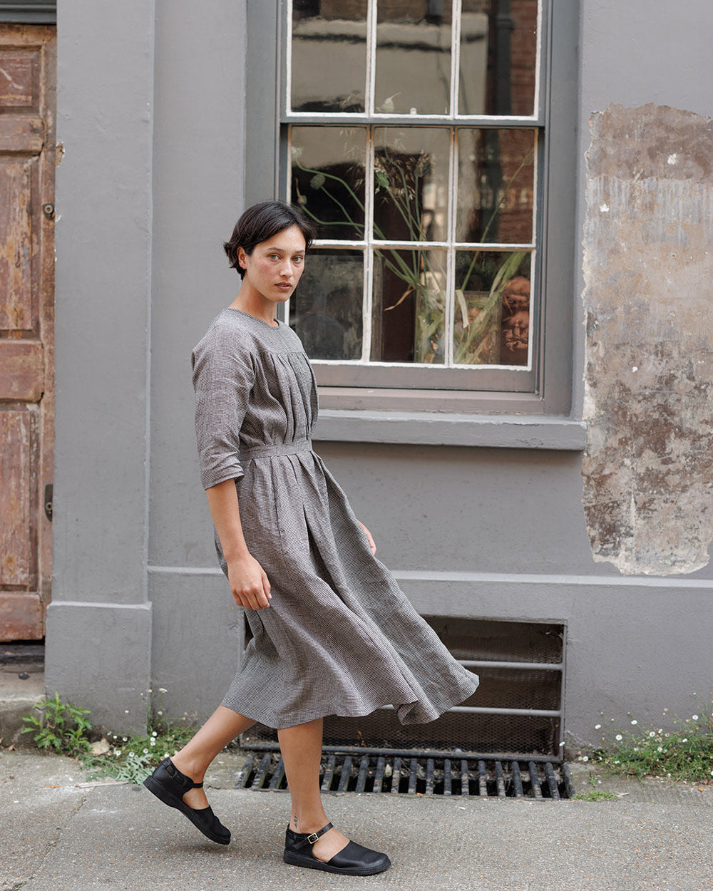 model in a loose, flowing black check linen dress walks past old, georgian house