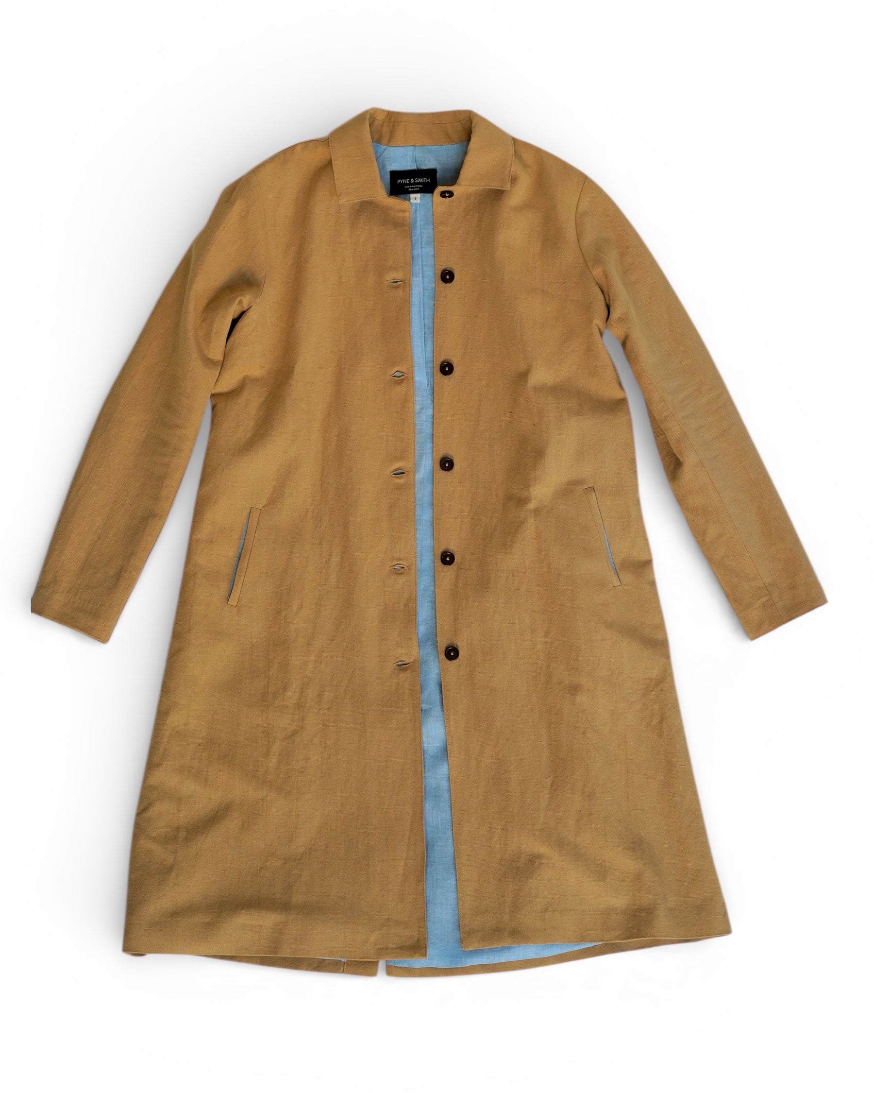 The Coat No.11 in Lark Tan Cotton Linen Canvas by Pyne and Smith Clothiers features an A-line silhouette, black buttons, side pockets, and a light blue inner lining, displayed flat against a white background.