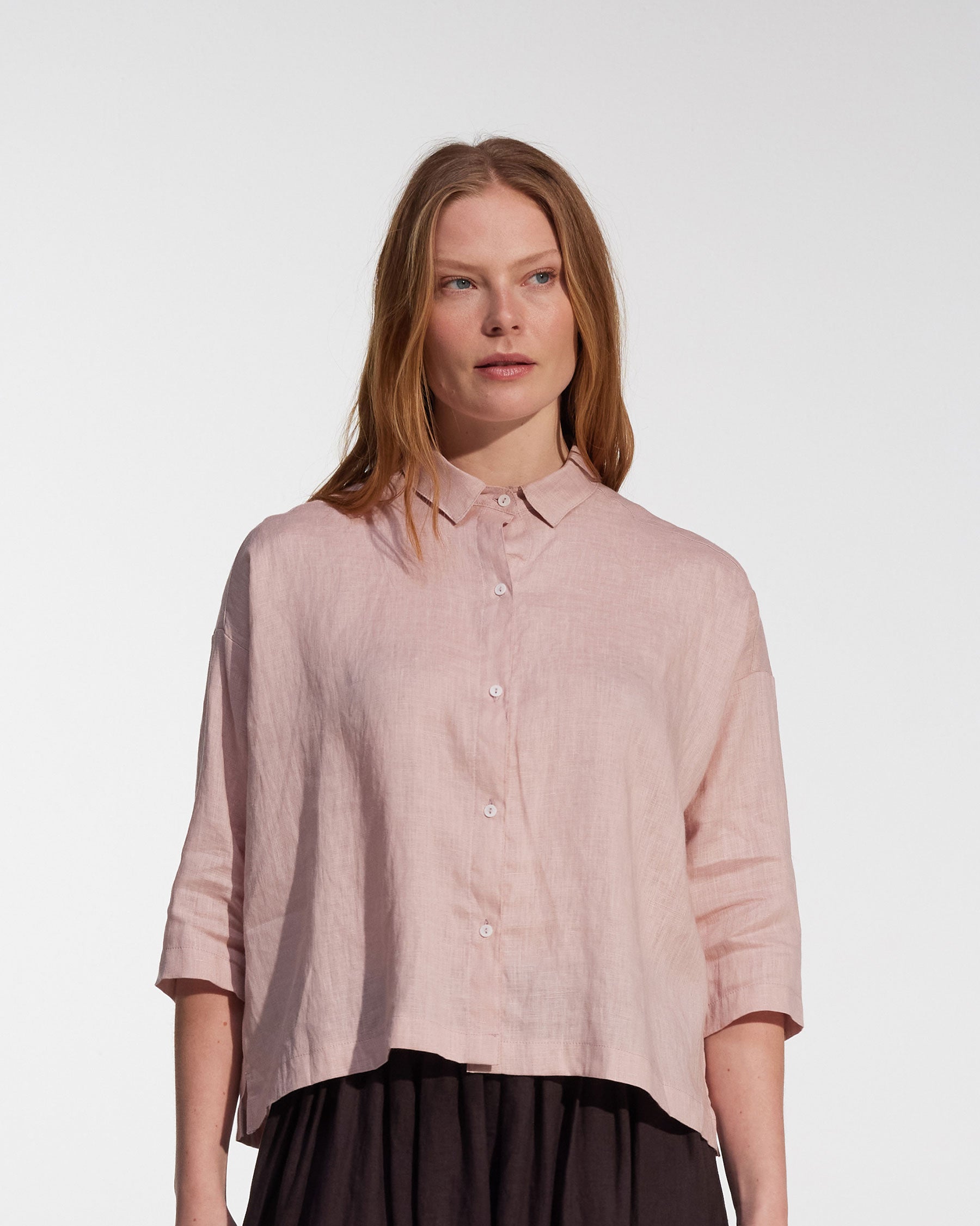 A woman with straight, light brown hair is wearing the Pyne and Smith Clothiers Boxy Cropped Linen Blouse No.22 in Sepia Rose. She stands against a plain, light background.