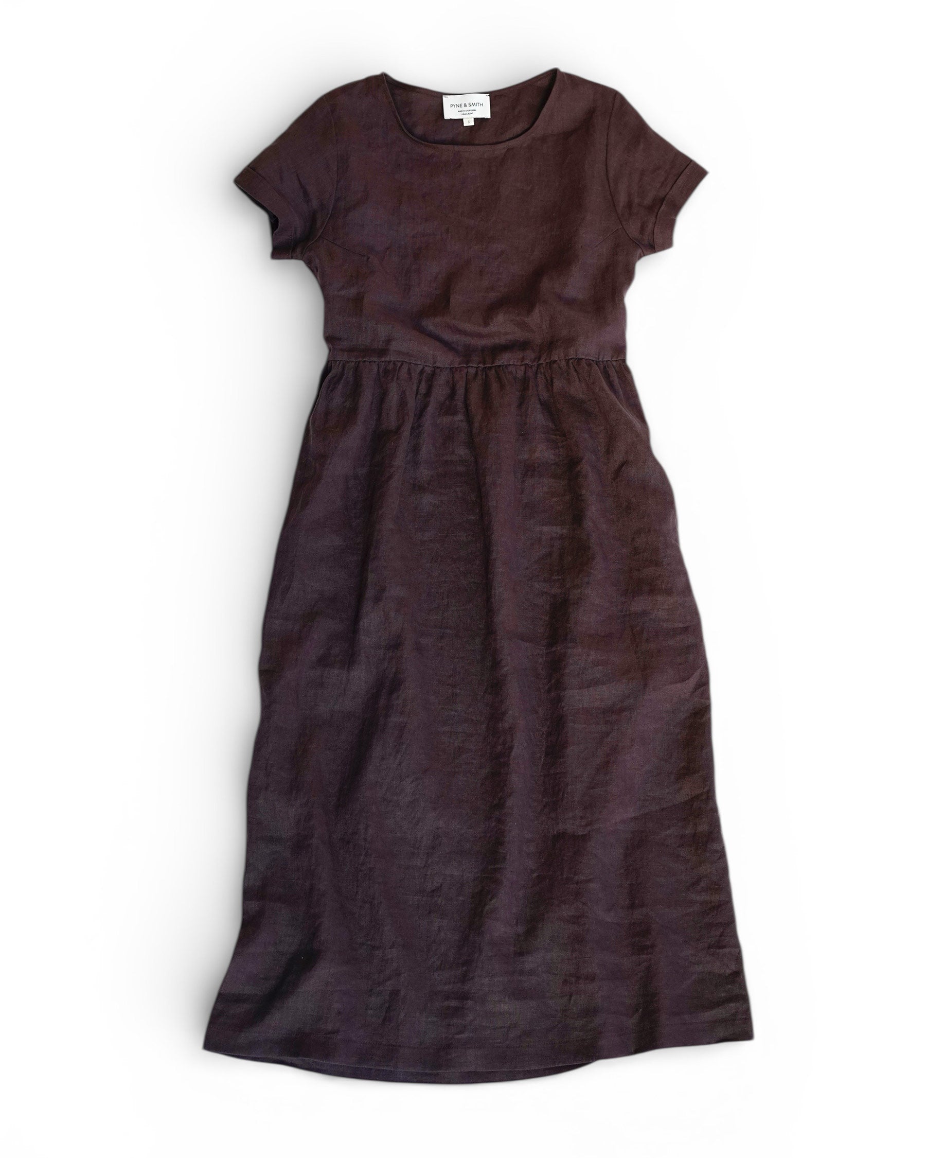 The Pyne and Smith Clothiers No.17 Full Length Linen Tea Dress in Chocolate Plum, with short sleeves, fitted bodice, gathered waist, and round neckline, is shown laid flat on a white background.