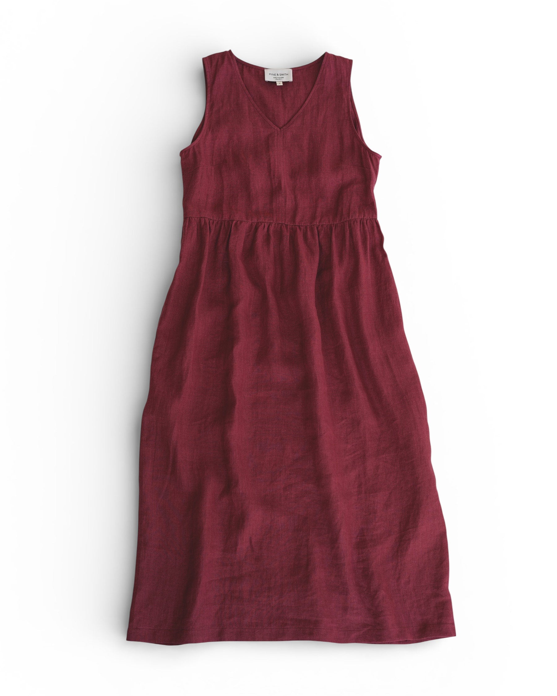 The No.21 V Neck Sleeveless Linen Dress in Roan by Pyne and Smith Clothiers is an ankle-length, raspberry red dress made of European flax linen with a V-neckline and gathered waist, shown laid flat on a white background.