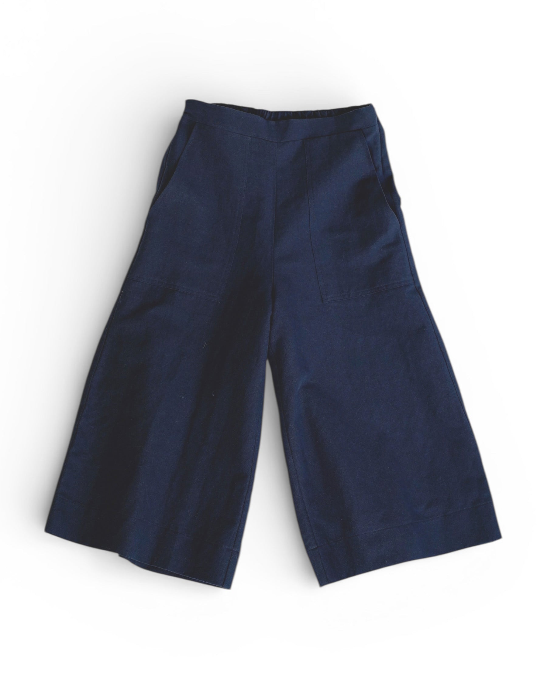Pyne and Smith Clothiers’ Canvas Cropped Trousers No.17 in Ink Blue are high-rise, wide-leg cotton linen trousers with an elastic waistband and front patch pockets, shown laid flat on a white background.