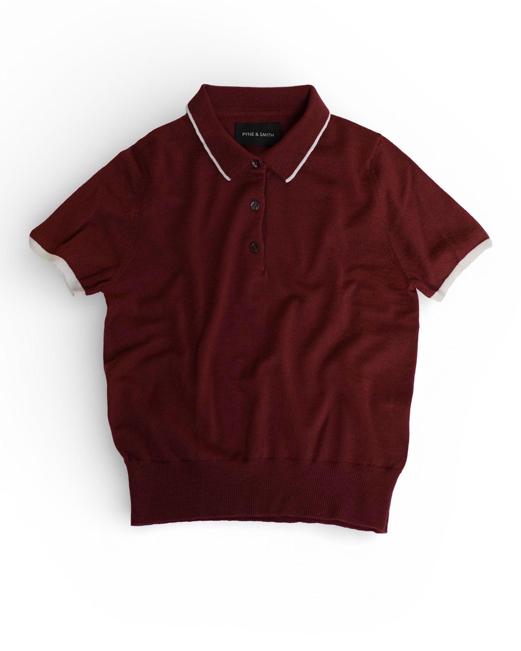 The Merino Polo Shirt in Rosso by Pyne and Smith Clothiers is a slim fit, short-sleeve maroon polo with white trim on the collar and sleeve cuffs, extra fine merino wool fabric, and three neck buttons, shown flat on a white background.