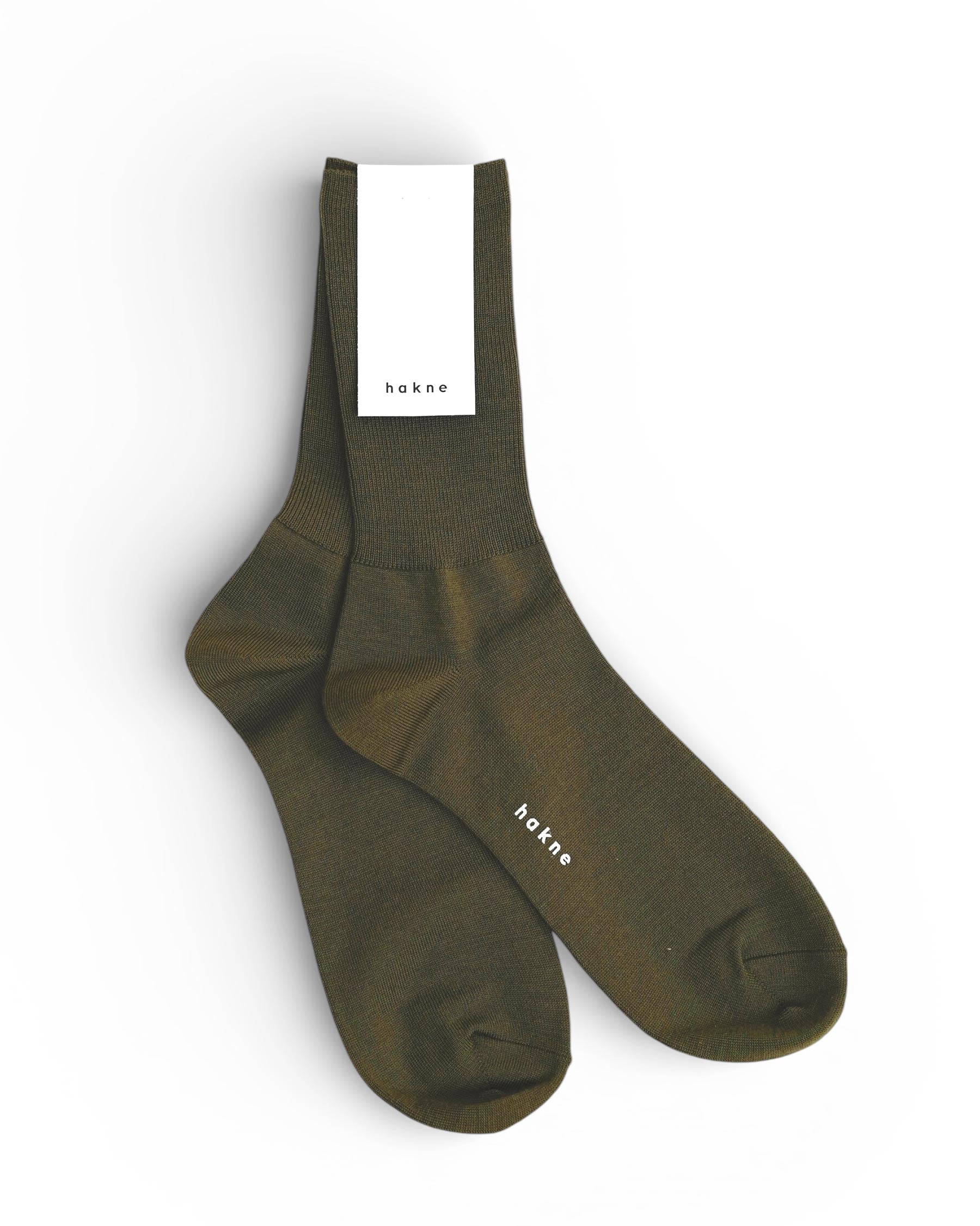 A pair of Merino Wool Ribbed Socks in green by Pyne and Smith Clothiers, featuring a white label at the top and banded text near the toes. The socks are displayed flat on a white background.