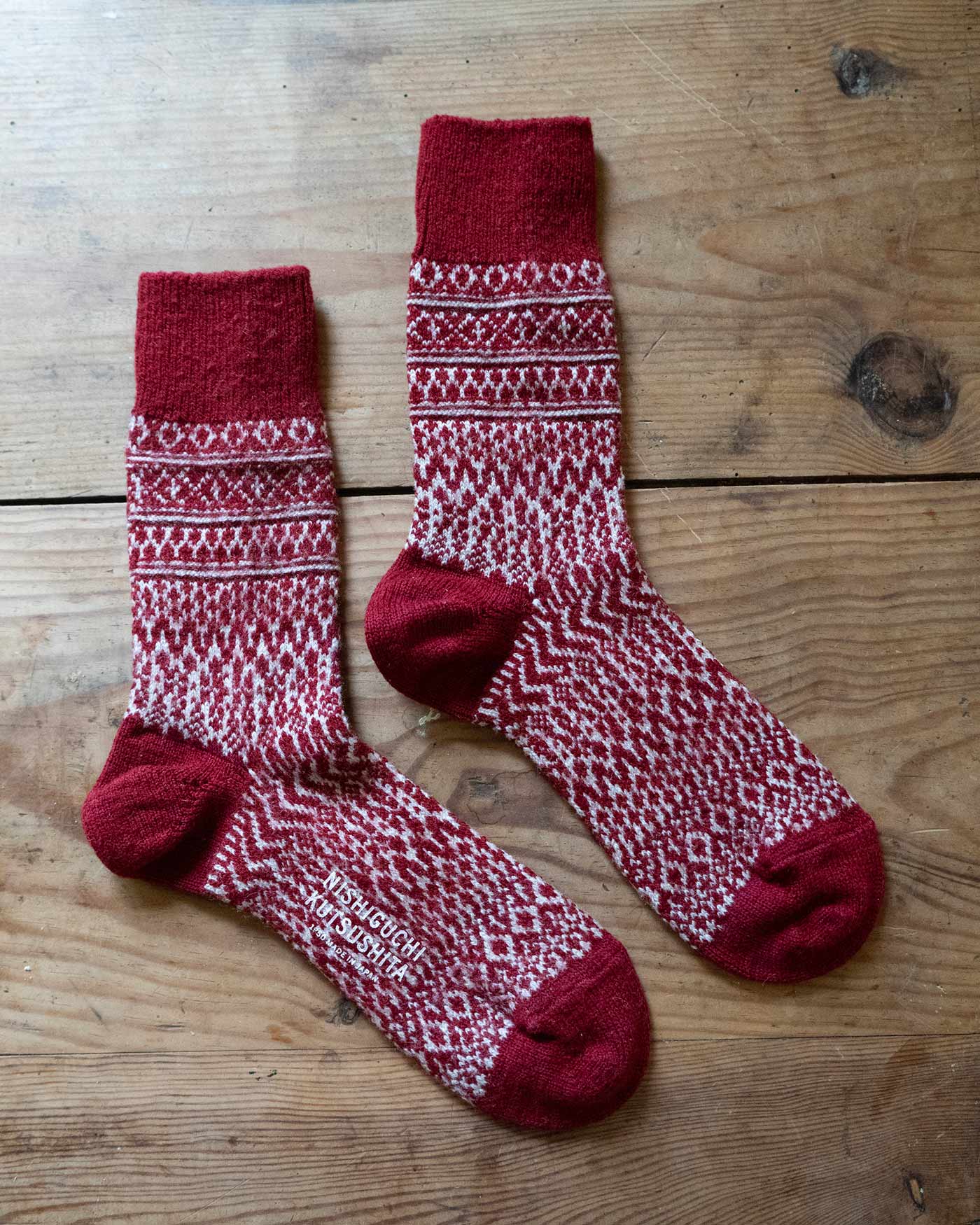 The Wool Jacquard Socks in Wine by Pyne and Smith Clothiers feature cosy red and white geometric patterns with solid red toes, heels, and cuffs, offering extra warmth for winter.