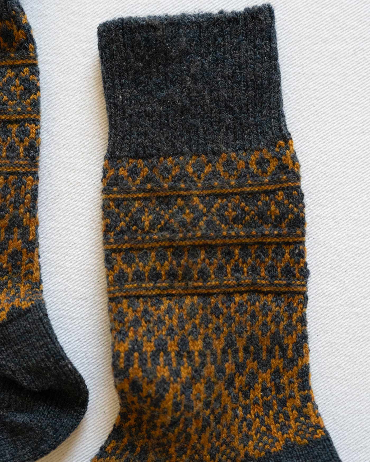 The Wool Jacquard Socks in Navy by Pyne and Smith Clothiers feature a cozy geometric and diamond pattern on a dark base—ideal for winter wool sock lovers.